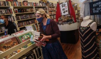 A photo of a woman working in a small retail store wearing a mask.