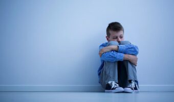 Photo of a boy alone sitting with his arms wrapped around his knees.
